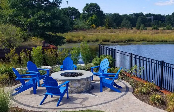 Blue chairs surrounding stone firepit on stone patio overlooking water